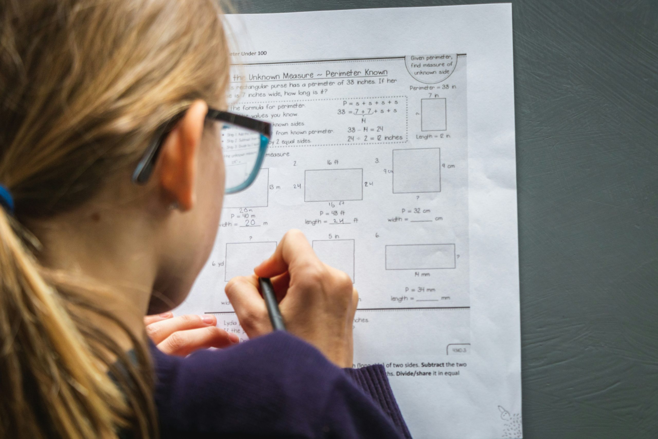 view of young girl with glasses from behind working on mathematics school work